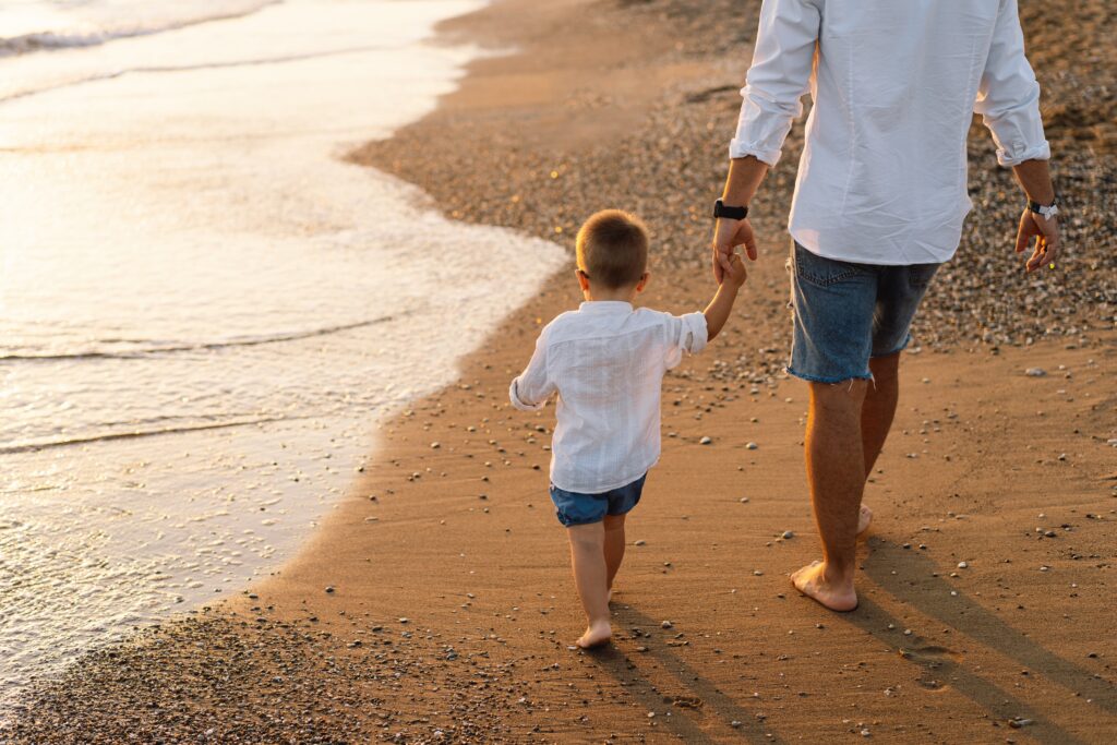 Father and baby play on the beach. Dad and him Child together enjoying sunset.